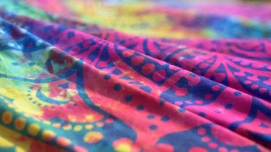 Parlak renkli kumaşlı etnik model mandala rüzgarda dalgalanıyor. Yakın plan. Parlak mavi, pembe, sarı ve morumsu arkaplan. Kumaş örtü rüzgarla sallanıyor. Yavaş çekim.