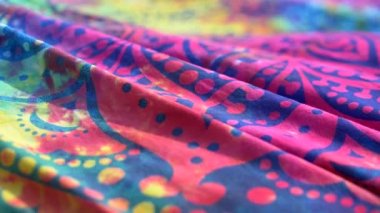 Parlak renkli kumaşlı etnik model mandala rüzgarda dalgalanıyor. Yakın plan. Parlak mavi, pembe, sarı ve morumsu arkaplan. Kumaş örtü rüzgarla sallanıyor. Yavaş çekim.