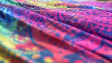 Parlak renkli kumaşlı etnik model mandala rüzgarda dalgalanıyor. Yakın plan. Parlak mavi, pembe, sarı ve morumsu arkaplan. Kumaş örtü rüzgarla sallanıyor. Yavaş çekim.