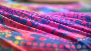 Parlak renkli kumaşlı etnik model mandala rüzgarda dalgalanıyor. Yakın plan. Parlak mavi, pembe, sarı ve morumsu arkaplan. Kumaş örtü rüzgarla sallanıyor. Yavaş çekim.