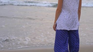 Sarışın, kısa saçlı, mavi geniş pantolonlu, zayıf, genç bir kız Alaaddin ve beyaz tişörtlü, sırtı seyirciye dönük olarak sahilde duruyor ve akşamları denize bakıyor..