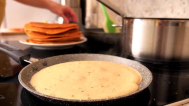 İnce bir gözleme tavada pişirilir, krepten yavaşça tepeye doğru buhar yükselir. Geleneksel Rus krepleri pişiriyorum. Yakın plan. Ağır çekim. Bir yığın gözlemenin arka planı.