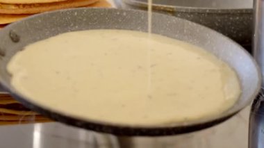 Ladle, Rus krepleri için parayı sıcak bir tavaya döker ve dişi el de hamuru tavaya dağıtır. Geleneksel Rus krepleri yapma süreci. Lezzetli Rus gözlemeleri pişiriyorum..