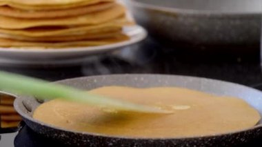 Dişi bir el, modern elektrikli bir fırında geleneksel Rus kreplerini pişiriyor, yeşil silikon spatulayla krepleri deviriyor ve üzerine tereyağı sürüyor. Rus gözlemesi pişiriyorum..