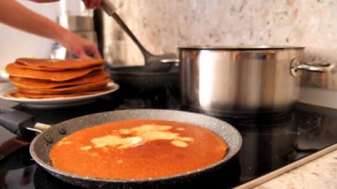 Ladle, Rus krepleri için parayı sıcak bir tavaya döker ve dişi el de hamuru tavaya dağıtır. Geleneksel Rus krepleri yapma süreci. Lezzetli Rus gözlemeleri pişiriyorum..