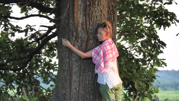 一个年轻的白人女人在公园里抱着一棵橡树树干 带着幸福和安静的微笑 低声说着什么 许个愿 大自然的力量 大自然的魔力 — 图库视频影像