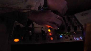 Kot ceketli DJ 'in elleri. Bulanık renkli ışıklar yanıp sönüyor. DJ mikserde renkli bulanık arkaplanda müzik çalıyor. 4K video.