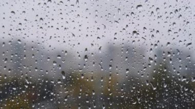 Pencerede yağmur damlaları. Pencereden bir damla yağmur akıyor. Arka planda bulanık binalar olan cam camlarına su damlaları ya da yağmur damlaları. Üzüntü, özlem, donukluk, sonbahar depresyonu, kasvet..