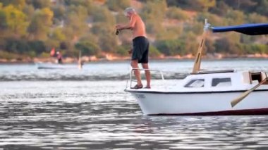 Hırvatistan, Marina, 29 Eylül 2019. Yaşlı bir adam ve kadın beyaz bir kayıkla yelken açıyorlar, bir kadın kürek çekiyor, bir erkek yengeçleri yakalamak için tuzak kuruyor ve avlarını kontrol ediyor..