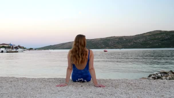 Ein Junges Mädchen Blauen Badeanzug Und Langen Blonden Haaren Sitzt — Stockvideo