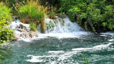 Krka Ulusal Parkı 'nda güzel bir dere yavaşça akar. Şelaleler Krka, Ulusal Park, Dalmaçya, Hırvatistan. Nehir ve akıntı yavaş ilerliyor. Şelale ve suyun yavaş çekim videosu.