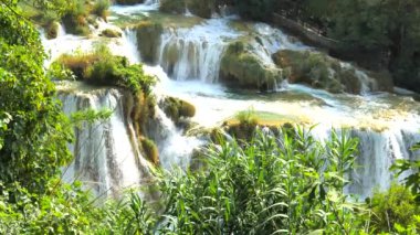 Şelaleler Krka, Ulusal Park, Hırvatistan. Ağaçlar ve çimenler arasındaki Krka Milli Parkı 'nda şelale çağlayanı gibi güzel nehirler yavaşça akar. Suyun, nehrin, akıntının, şelalenin yavaş çekim videosu.