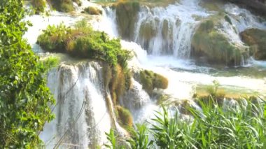 Şelaleler Krka, Ulusal Park, Hırvatistan. Ağaçlar ve çimenler arasındaki Krka Milli Parkı 'nda şelale çağlayanı gibi güzel nehirler yavaşça akar. Suyun, nehrin, akıntının, şelalenin yavaş çekim videosu.