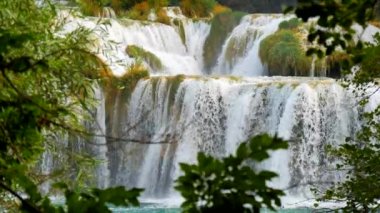 Şelaleler Krka, Ulusal Park, Hırvatistan. Ağaçlar ve çimenler arasındaki Krka Milli Parkı 'nda şelale çağlayanı gibi güzel nehirler yavaşça akar. Suyun, nehrin, akıntının, şelalenin yavaş çekim videosu.