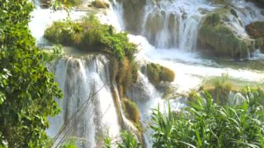 Şelaleler Krka, Ulusal Park, Hırvatistan. Ağaçlar ve çimenler arasındaki Krka Milli Parkı 'nda şelale çağlayanı gibi güzel nehirler yavaşça akar. Suyun, nehrin, akıntının, şelalenin yavaş çekim videosu.