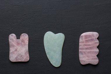 Yüze ve vücuda masaj için aletler. Doğal taşlar, mineral gül kuvars, siyah arka planda beyaz yeşim taşı, taş terapisi. Çin geleneksel masajı. Gouacha kazıyıcılarıyla. Metnin için boşluk kopyala.