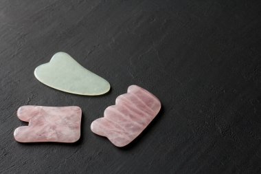 Yüze ve vücuda masaj için aletler. Doğal taşlar, mineral gül kuvars, siyah arka planda beyaz yeşim taşı, taş terapisi. Çin geleneksel masajı. Gouacha kazıyıcılarıyla. Metnin için boşluk kopyala.