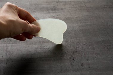 Genç kadın eli, yüz masajı için gouacha kazıyıcısı tutuyor. Vücut, doğal beyaz yeşim taşı, siyah arka plan. Güzellik ve gençlik için terapi masajı. Metnin için boşluk kopyala.