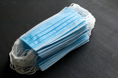 Korunmak için birçok mavi tıbbi maske siyah arka planda yatar. Cerrahi maske. Ağız ve burnu kapamak için tipik cerrahi maske. Prosedür maske bakterisi. Koronavirüse karşı koruma kavramı.