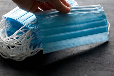 Mavi tıbbi maske elinde. Koruma için tek kullanımlık maskeler siyah arka planda yatar. Ağız ve burnu kapamak için tipik cerrahi maske. Prosedür maske bakterisi. Koronavirüse karşı koruma kavramı.