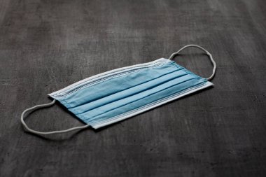 Mavi tıbbi maske elinde. Koruma için tek kullanımlık maske siyah arka planda. Ağız ve burnu kapamak için tipik cerrahi maske. Prosedür maske bakterisi. Koronavirüse karşı koruma kavramı.