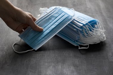 Elleri mavi tıbbi maske taşıyor. Koruma için tek kullanımlık maskeler siyah arka planda yatar. Ağız ve burnu kapamak için tipik cerrahi maske. Prosedür maske bakterisi. Koronavirüse karşı koruma kavramı.