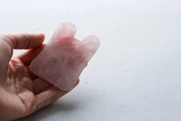 Massage of face and body. Female hand holds gouacha in its palm, made from natural stone mineral rose quartz. Therapeutic healing massage for beauty and youth of face, body. Copy space for your text.