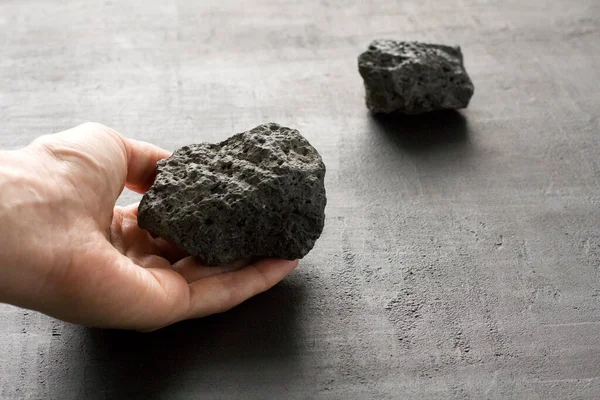 Female hand holds a black stone of lava and magma from the volcano Etna on the island of Sicily, Italy. Stone after the eruption of volcano. Natural black stone, mineral on black background, close-up.