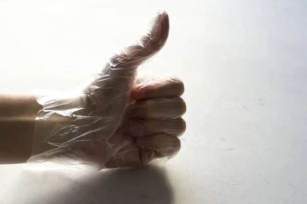 A hand in a transparent plastic transparent glove closeup lies on a light gray modern concrete background. The concept of protection against infection and coronavirus. Hand shows like.