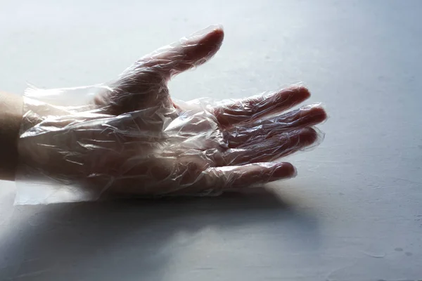 A hand in a transparent plastic transparent glove closeup lies on a light gray modern concrete background. The concept of protection against infection and coronavirus. Danger and protection.