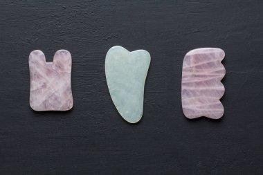 Yüze ve vücuda masaj için aletler. Doğal taşlar, mineral gül kuvars, siyah arka planda beyaz yeşim taşı, taş terapisi. Çin geleneksel masajı. Gouacha kazıyıcılarıyla. Metnin için boşluk kopyala.