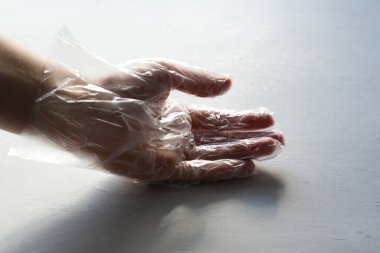 Şeffaf plastik şeffaf eldiven içindeki bir el açık gri, modern beton arka planda yatar. Enfeksiyon ve koronavirüse karşı koruma kavramı. Tehlike ve koruma.