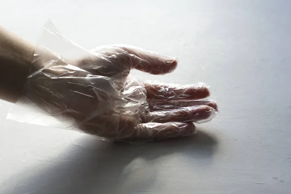 A hand in a transparent plastic transparent glove closeup lies on a light gray modern concrete background. The concept of protection against infection and coronavirus. Danger and protection.