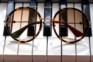Moscow, Russia, May 20, 2020. Gucci sunglasses are popular high-end brand, created for men, women, with round dark lenses lie on black and white piano keys. Image shows Gucci logo. clipart