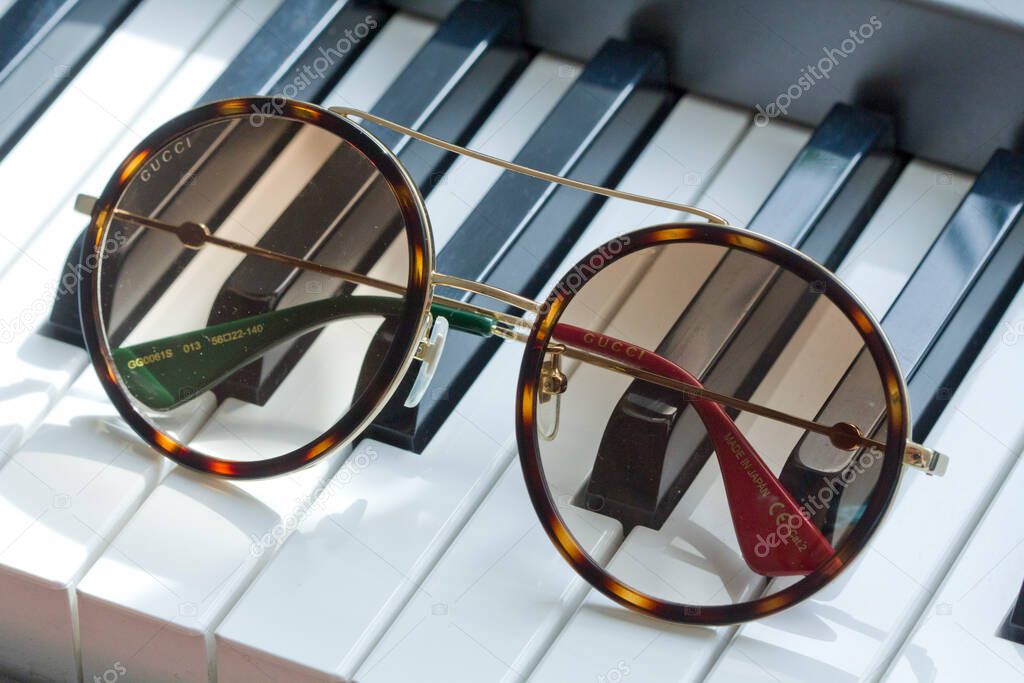 Moscow, Russia, May 20, 2020. Gucci sunglasses are popular high-end brand, created for men, women, with round dark lenses lie on black and white piano keys. Image shows Gucci logo.