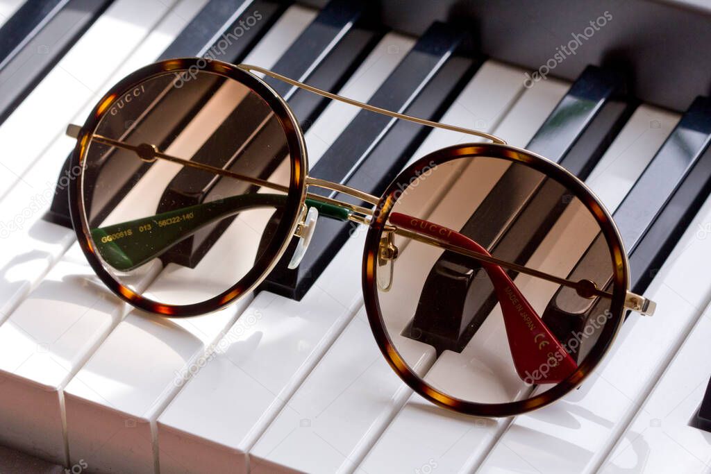 Moscow, Russia, May 20, 2020. Gucci sunglasses are popular high-end brand, created for men, women, with round dark lenses lie on black and white piano keys. Image shows Gucci logo.