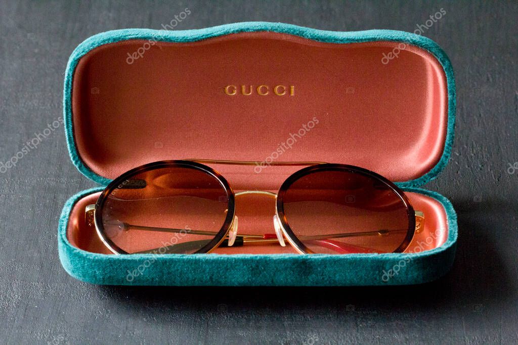 Moscow, Russia, May 20, 2020. Gucci sunglasses are popular high-end brand, created for men, women, with round dark lenses lie on background of green case, on black background. Image shows Gucci logo.