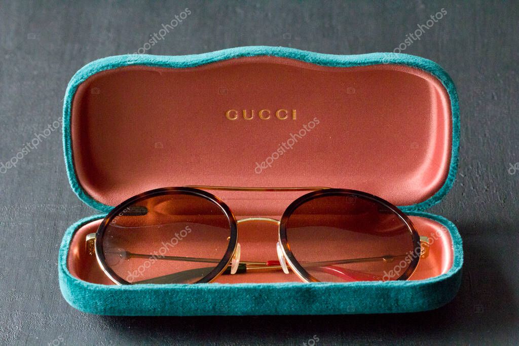 Moscow, Russia, May 20, 2020. Gucci sunglasses are popular high-end brand, created for men, women, with round dark lenses lie on background of green case, on black background. Image shows Gucci logo.