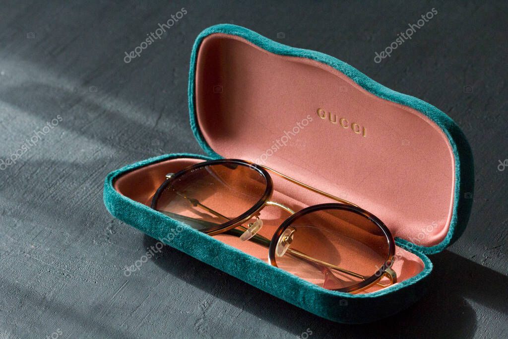 Moscow, Russia, May 20, 2020. Gucci sunglasses are popular high-end brand, created for men, women, with round dark lenses lie on background of green case, on black background. Image shows Gucci logo.