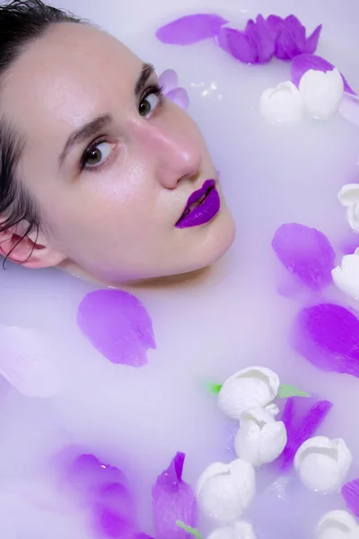 Κορίτσι μοντέλο μόδας με βιολετί μακιγιάζ σε λουτρό γάλακτος με βιολετί λουλούδια — Φωτογραφία Αρχείου