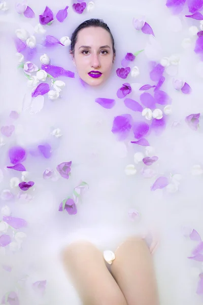 Chica modelo de moda con maquillaje violeta en baño de leche con flores violetas —  Fotos de Stock