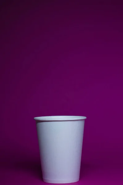 An empty white paper cup on a pink background