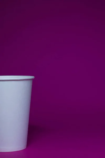 An empty white paper cup on a pink background
