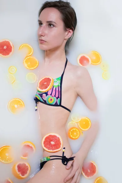 밝은 수영복을 입은 여인이 오렌지 , 레몬 및 포도와 함께 목욕을 한다. 패션 모델, 스파 및 피부 관리 개념. — 스톡 사진