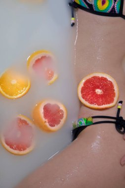 Süt banyosunda portakallı, limonlu, greyfurtlu kadın vücudu. Moda modeli, kaplıca ve cilt bakımı konsepti