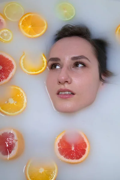 Retrato de mujer en baño de leche con naranjas, limones y pomelos. Modelo de moda, spa y concepto de cuidado de la piel . — Foto de Stock
