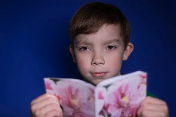 Portrét Devítiletého Blonďáka Jak Čte Knihu Květinách Modrém Pozadí — Stock fotografie