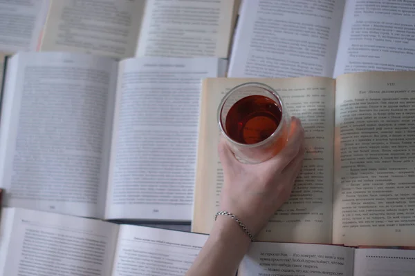Une main avec un bracelet en argent tenant une tasse de thé avec un double fond sur les pages de livres — Photo