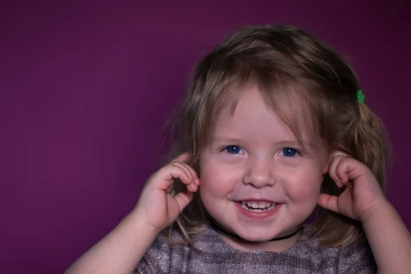 Portret van gelukkig een drie jaar oud blond meisje met blauwe ogen op een roze achtergrond — Stockfoto