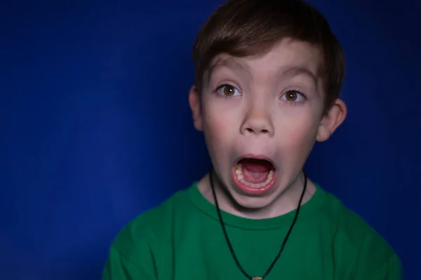 Portrait of a shocked nine year old blond boy on a blue background — Stock Photo, Image